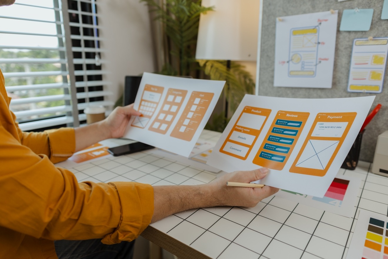 Designer reviewing wireframes and UI prototypes on paper.