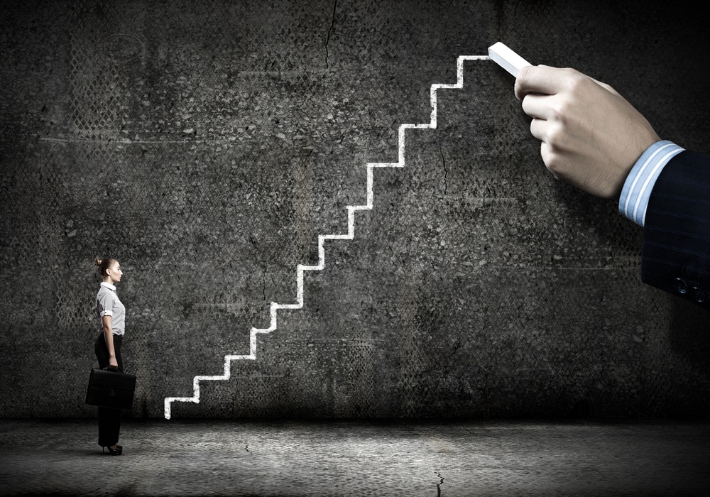 Businesswoman looking at a staircase drawn in chalk on a dark wall, symbolizing steps toward digital transformation.